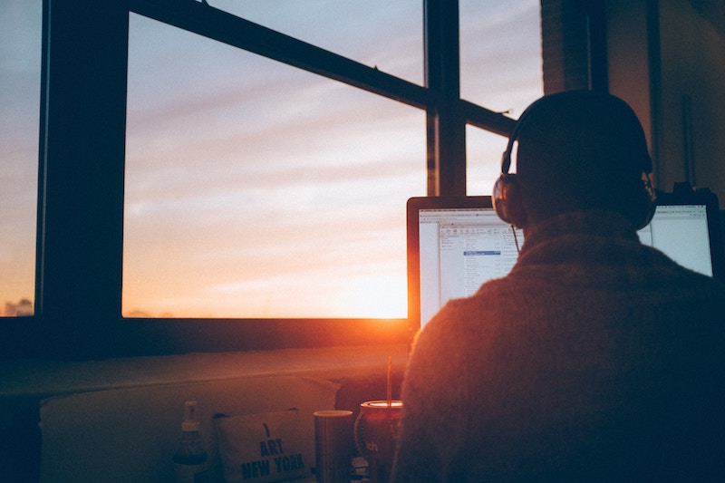 man at airport from behind using computer with sunset in window.