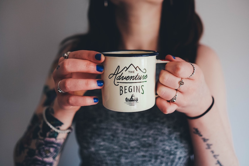 woman holding mug that reads the adventure begins