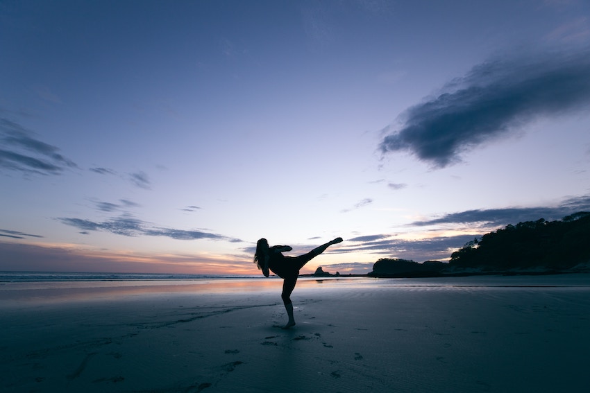 girl doing a roundhouse kick on the beach