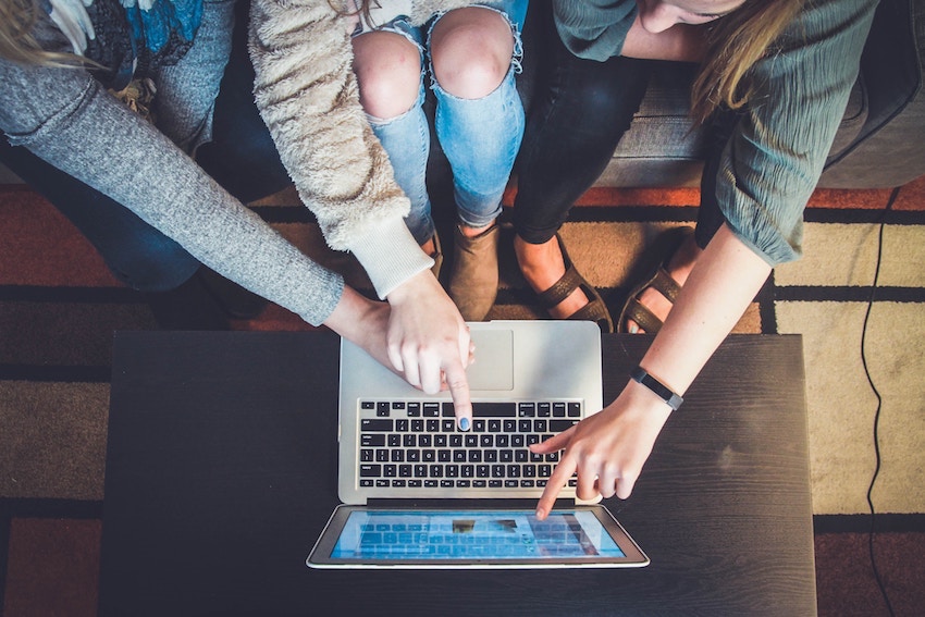 women sitting around computer and pointing at screen