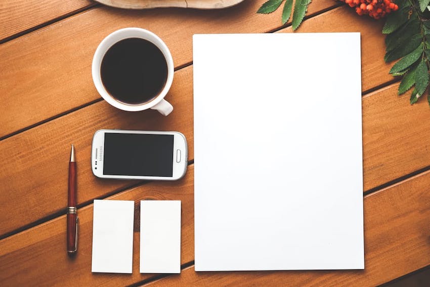 desk with blank paper art supplies post it notes and coffee on a wooden desk