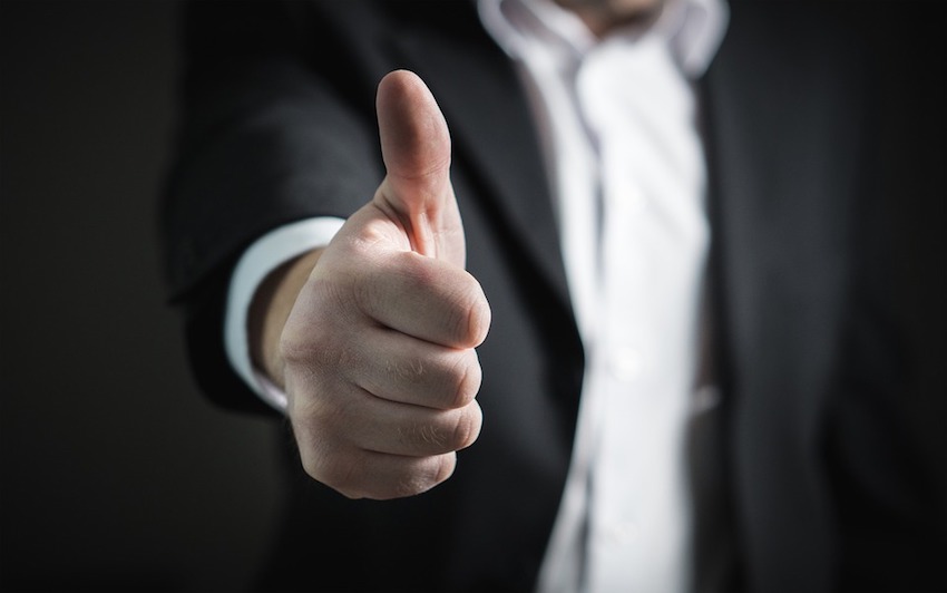 man in dark suit with focus on thumbs up in the foreground