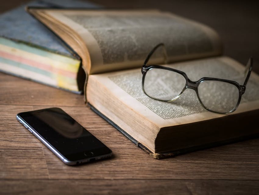 stack of books with glasses on top and smart phone laying next to them