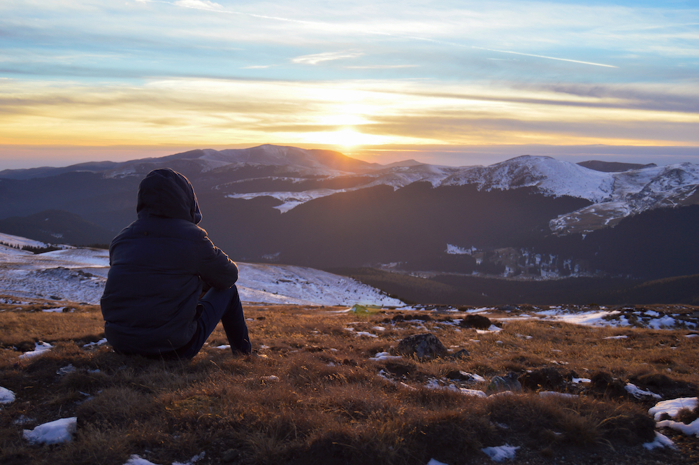 man sitting on edge of cliff looking out into horizon