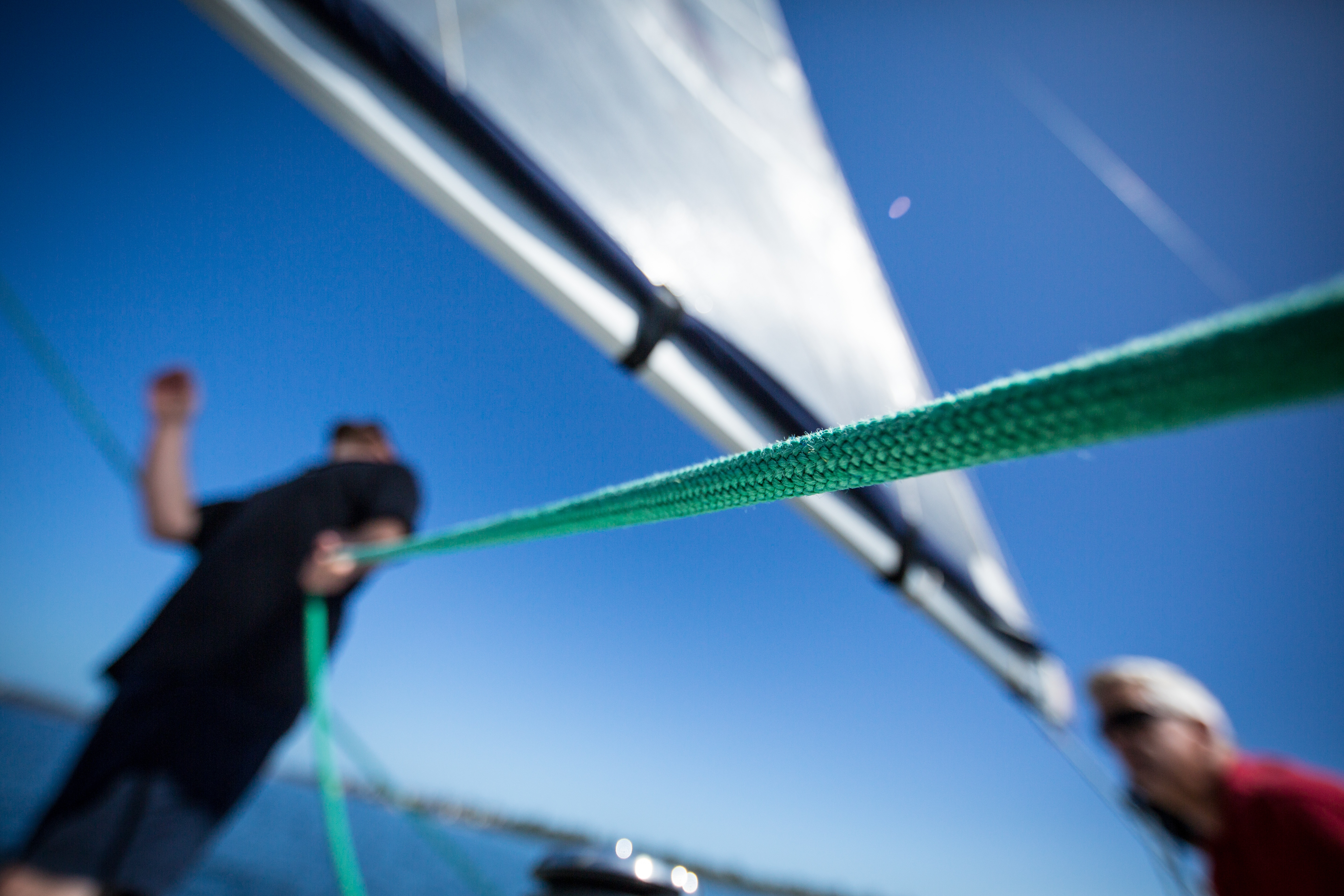 man pulling green rope on sailboat