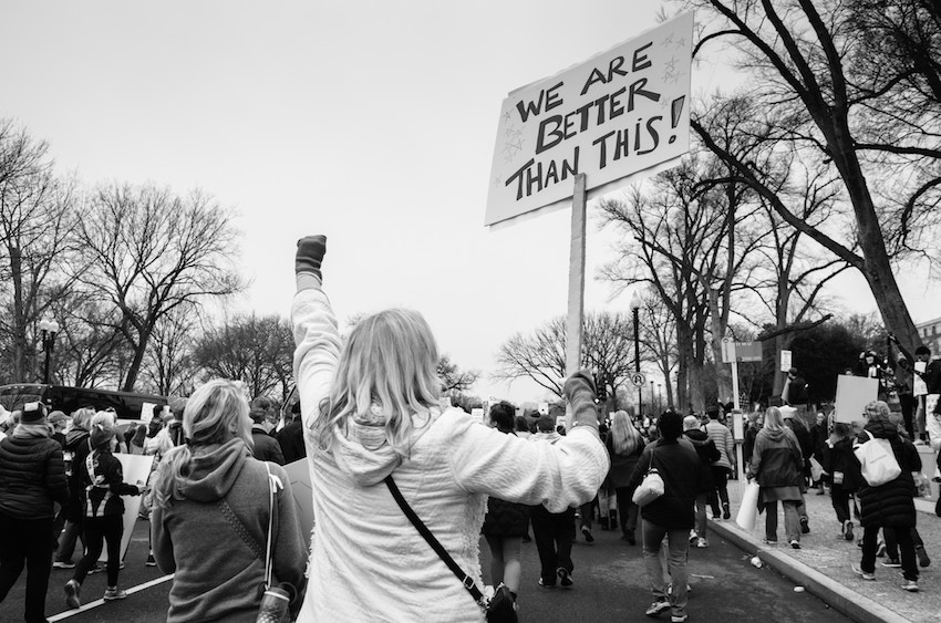 woman in protest with sign that reads we are better than this