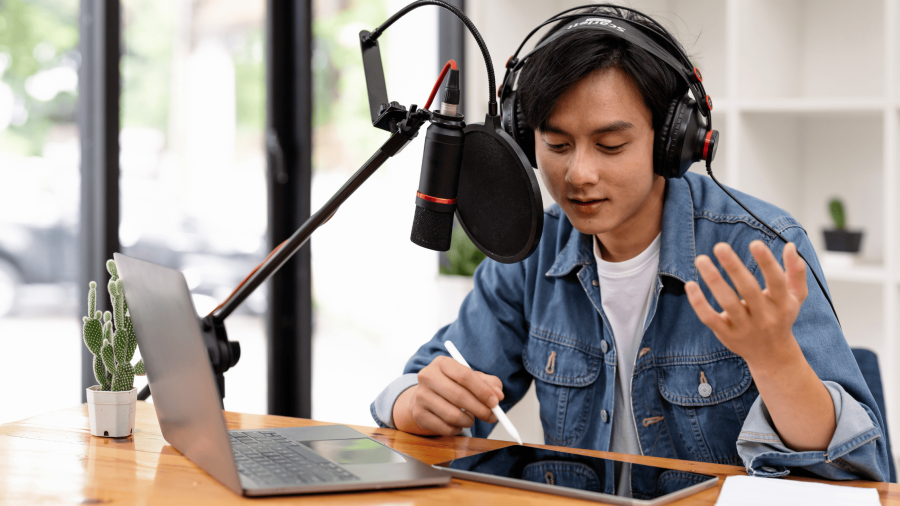 a person with headphones and a jean jacket holds a pen over a tablet while talking into a microphone