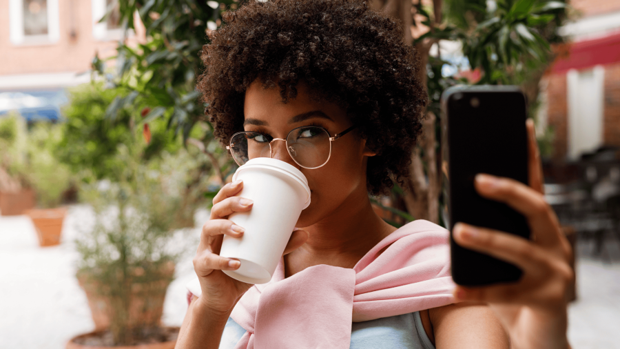 women looking at phone vertically while drinking coffee