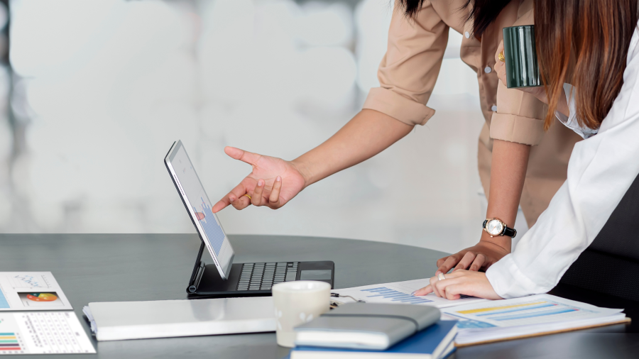 Two people leaning over a tablet with a keyboard and paper graphs.