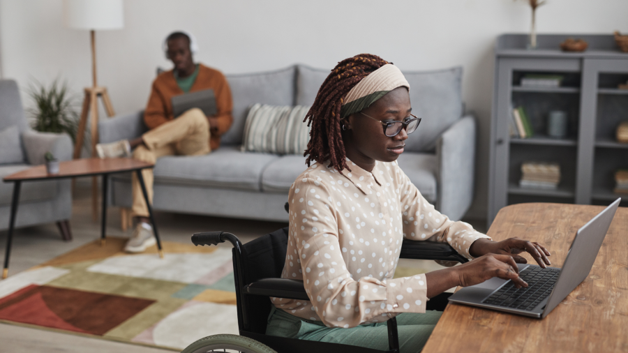 A black woman in a wheel chair working at a laptop in a living room.